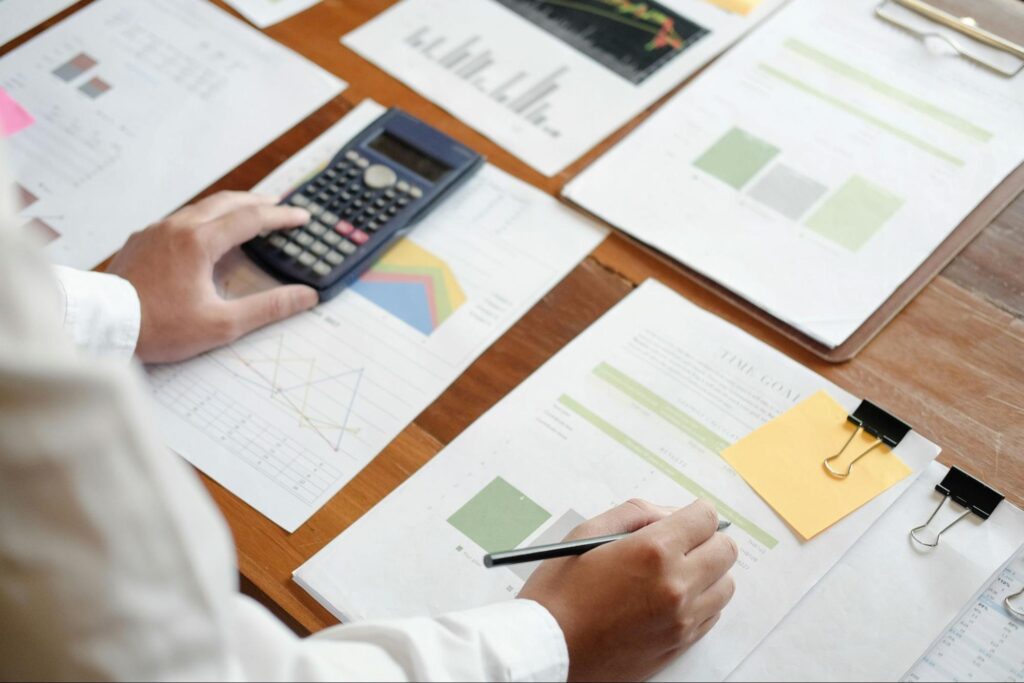 Photo of a man's arms as he sits at a desk. He's using a calculator and holding a pen while he looks at documents.