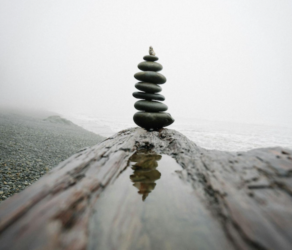 Rocks balancing on top of each other on a beach with the ocean in the background.