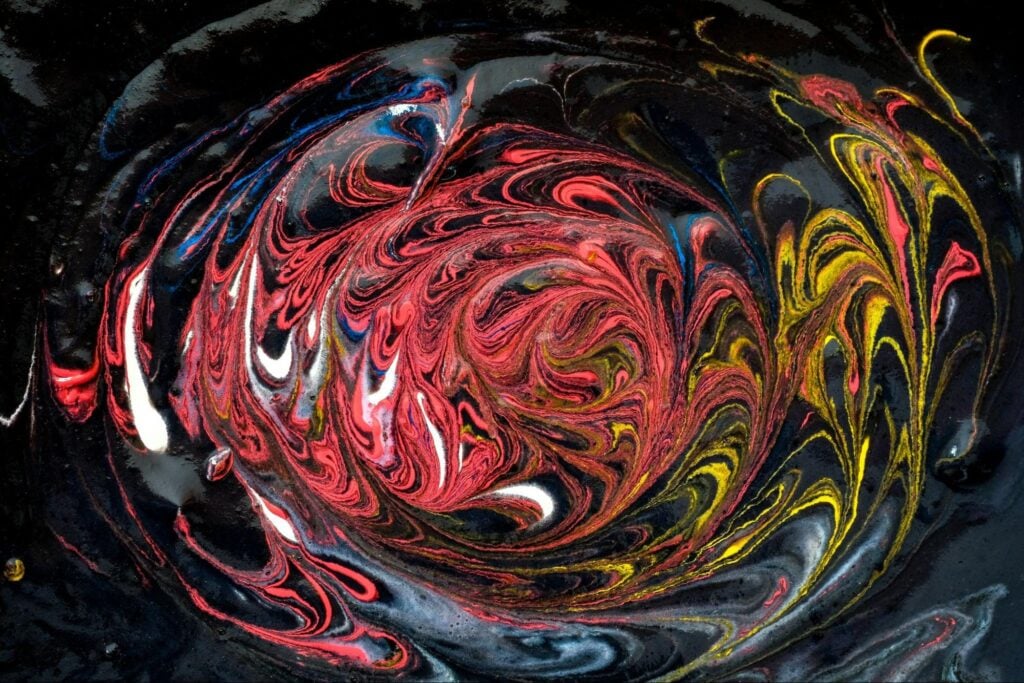 Red, yellow, blue, and gray paint swirl on a black background.